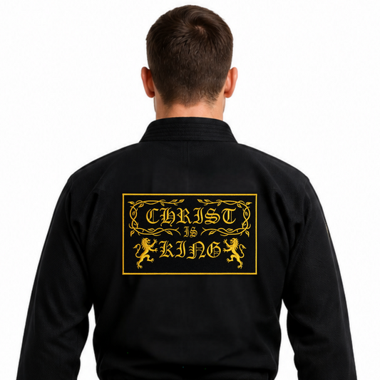 A man viewed from the back wearing a black martial arts gi with a black belt, featuring a large gold graphic on the back that reads 'CHRIST IS KING' with decorative borders and lions.
