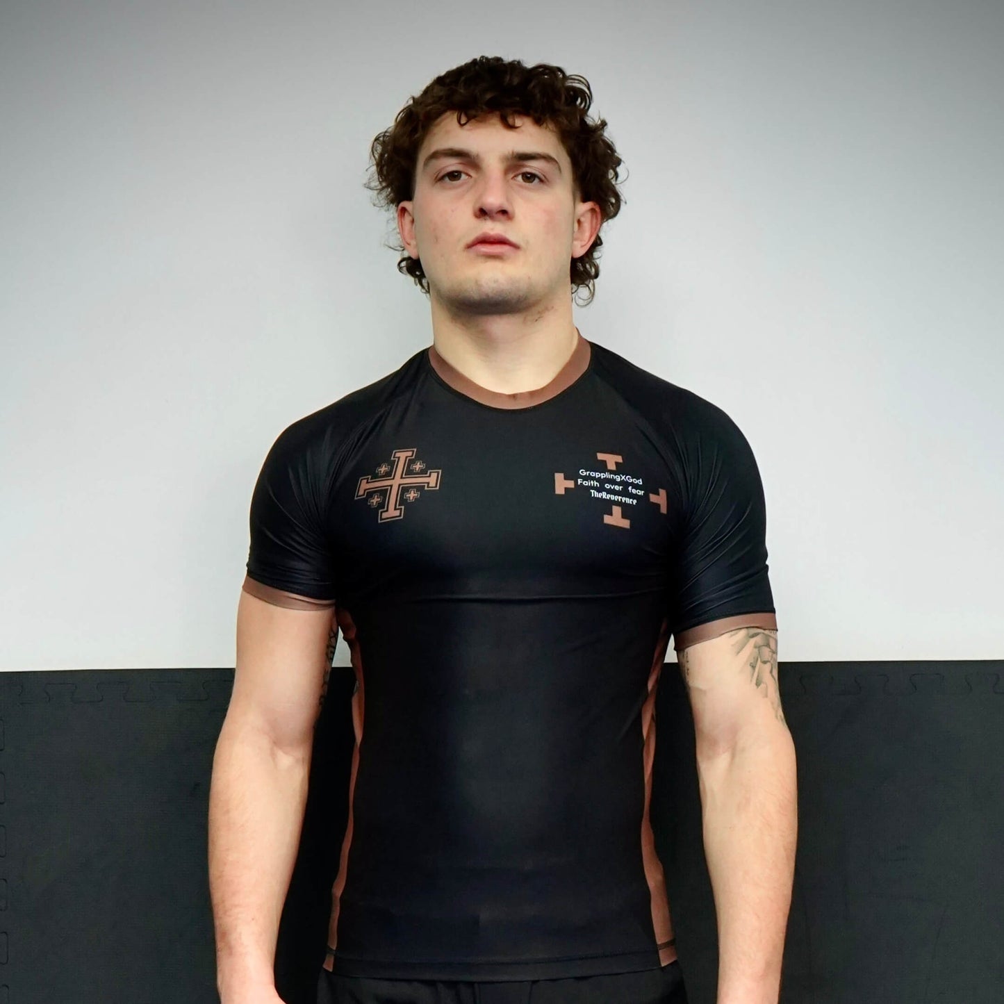 Person wearing a black athletic shirt with logos against a plain background
