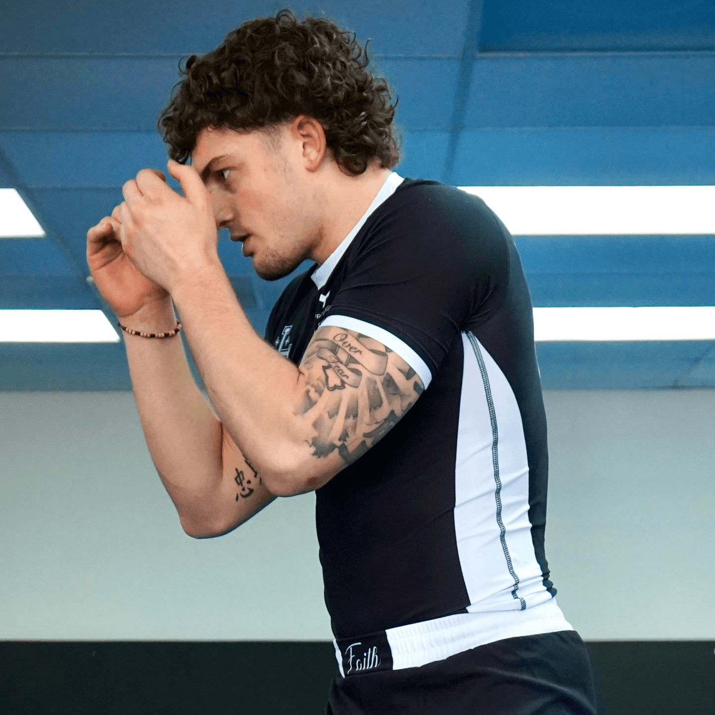 Man wearing black and white rashguard with cross designs in gym setting.