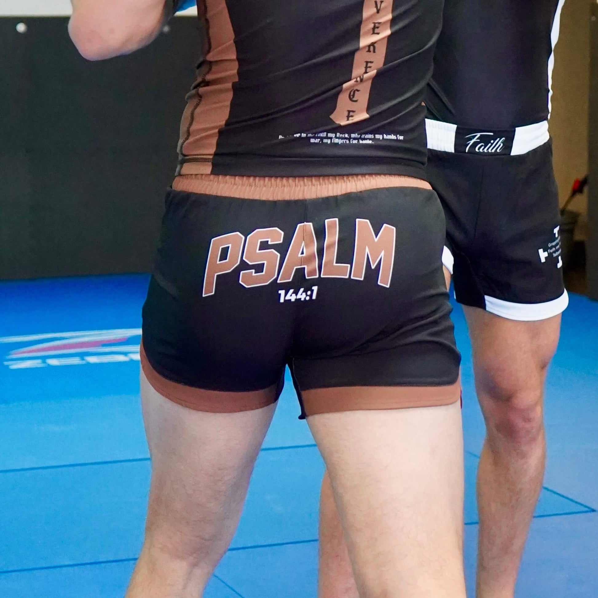 Person wearing black shorts with 'PSALM 144:7' printed on them, standing on a blue mat.