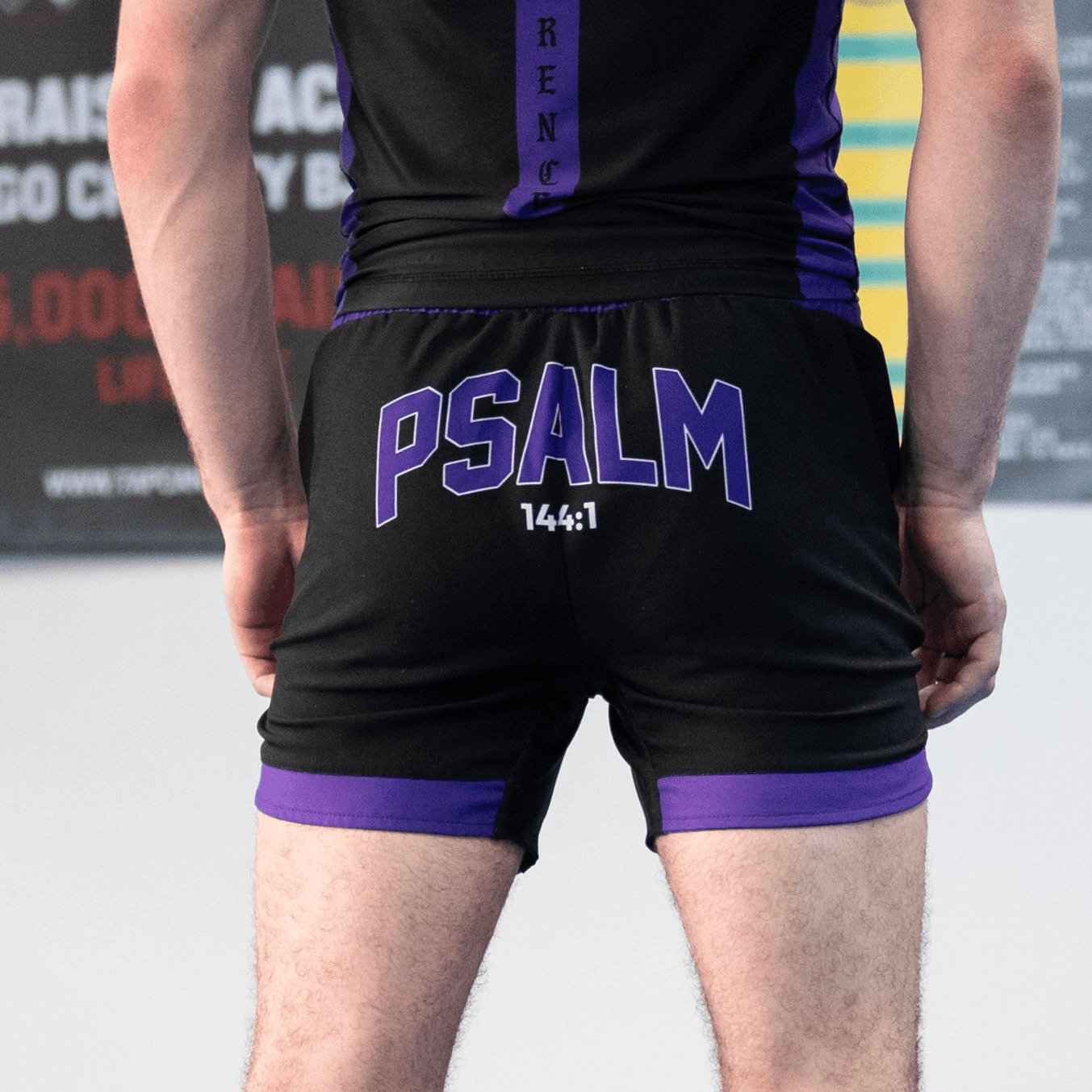Black athletic shorts with purple accents and 'PSALM 144:1' text on a person against a blurred background.
