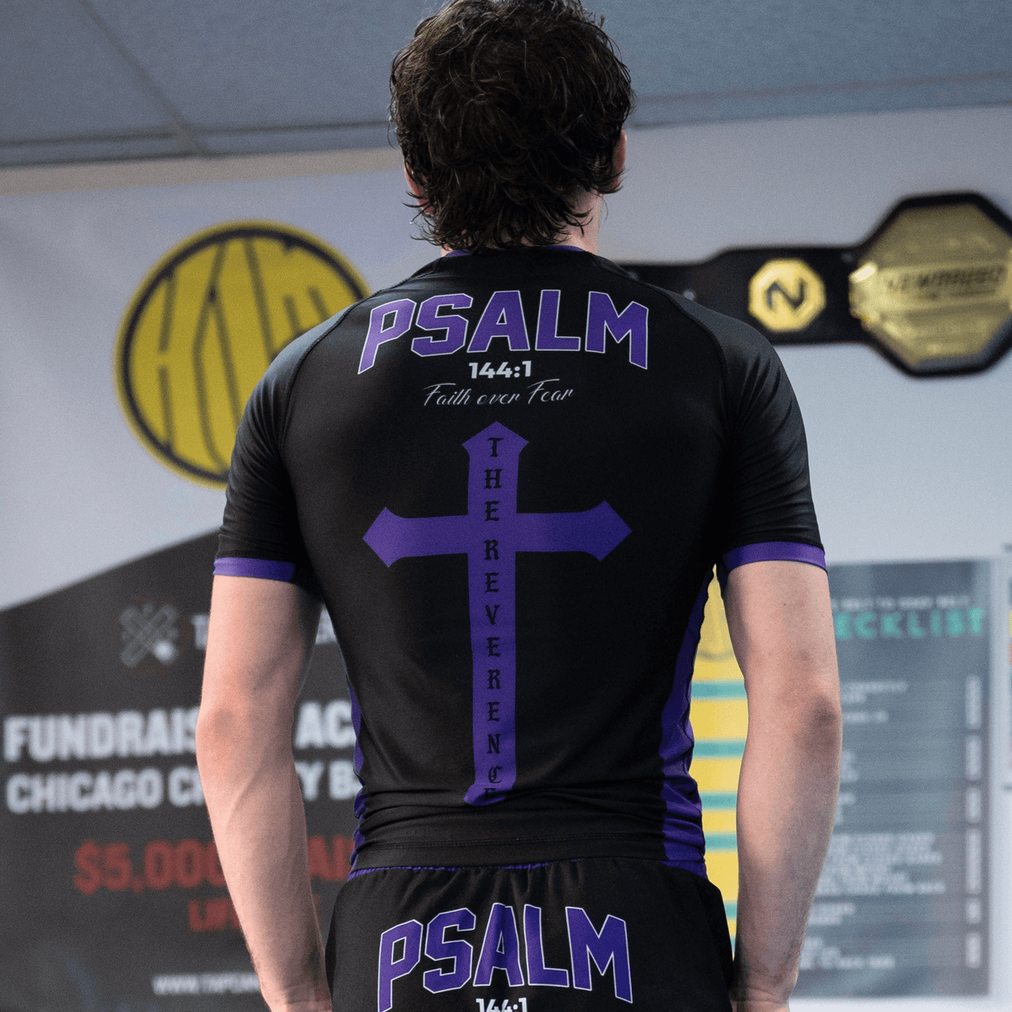 Man wearing black and purple rashguard with "PSALM" text and cross design on the back