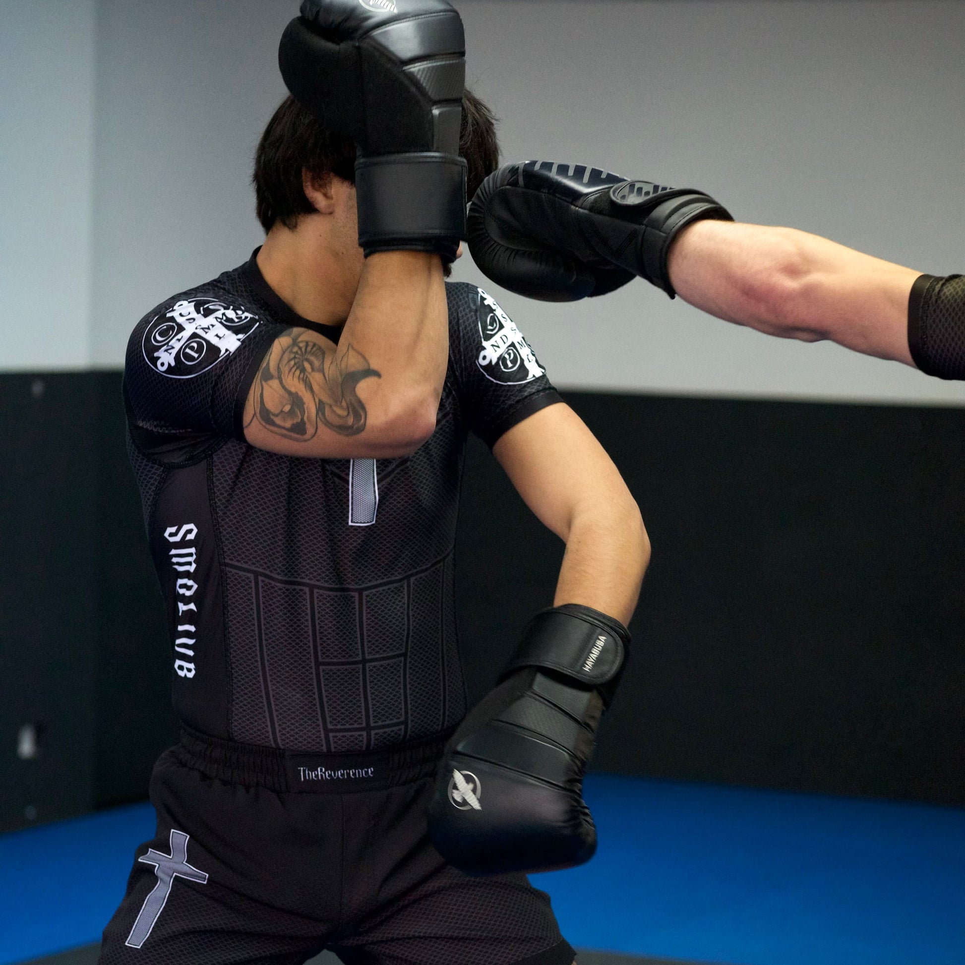 Person wearing black martial arts gear in a training stance on a blue mat.
