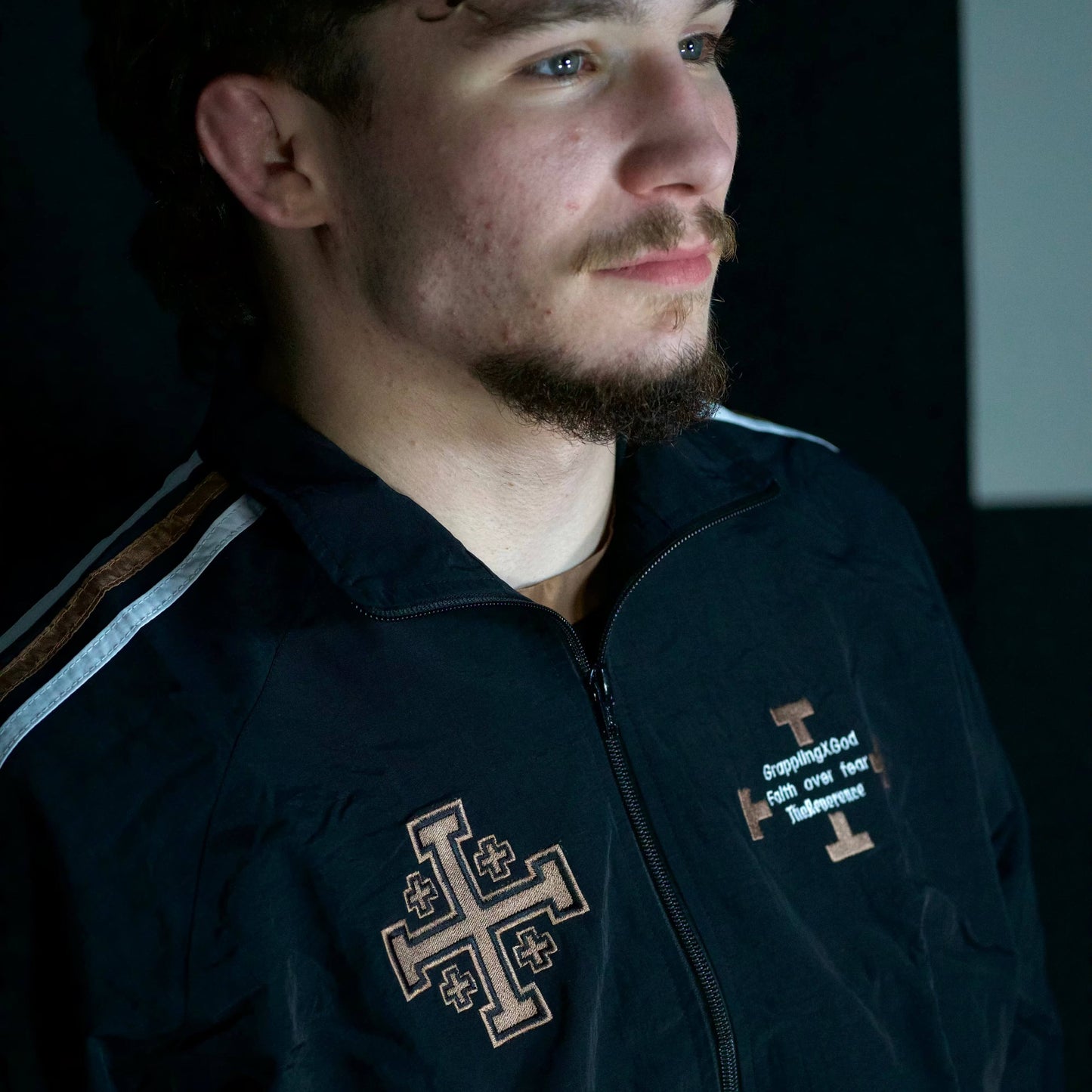 Man wearing a dark jacket with a cross emblem and text on a dark background