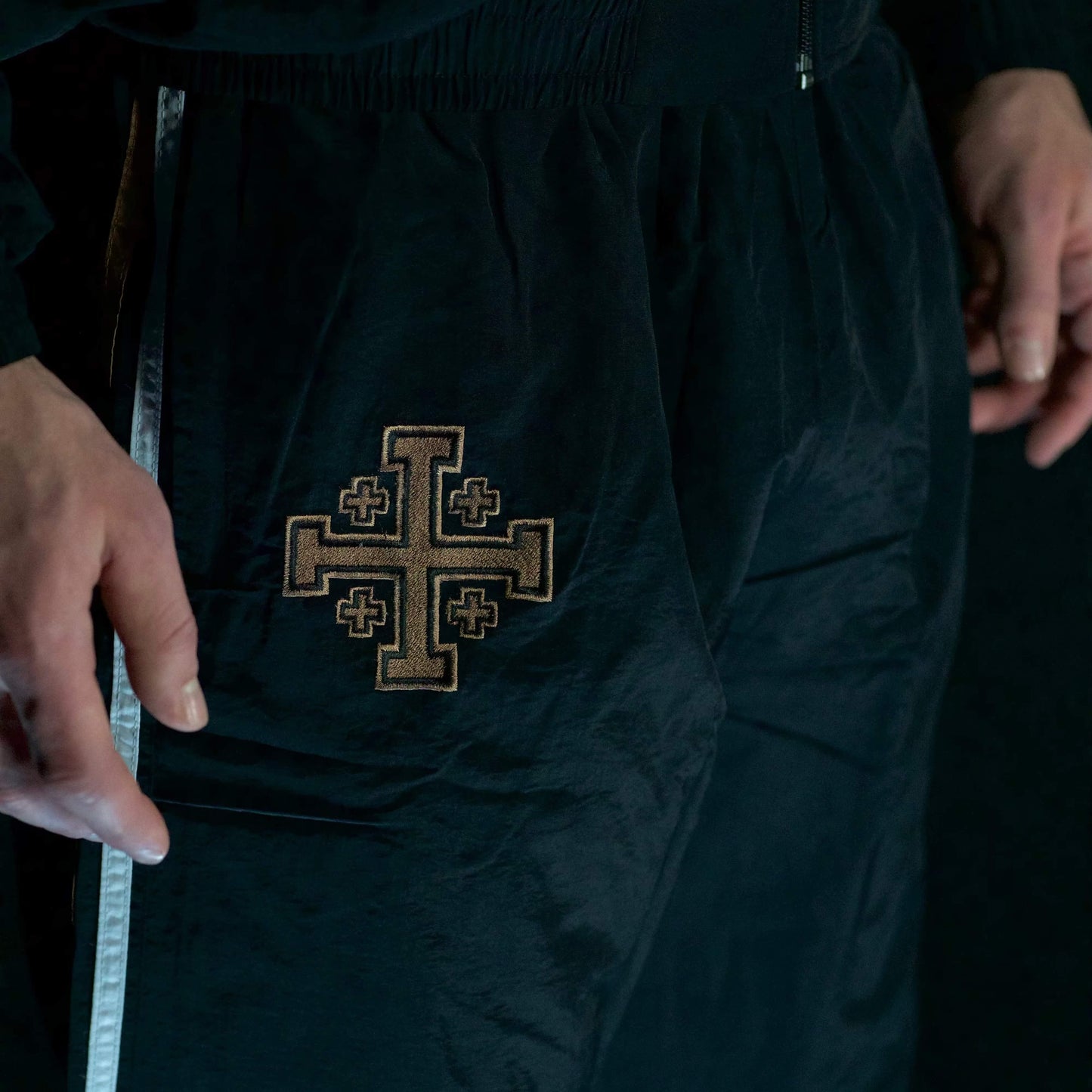 Black pants with an embroidered cross design on a dark background