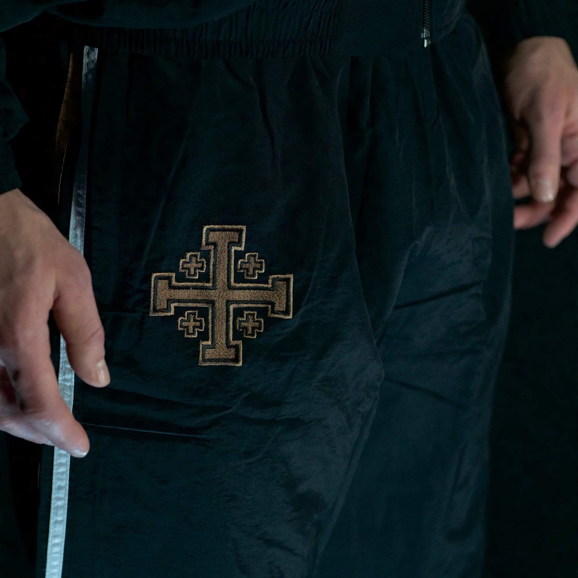 Black pants with an embroidered cross design on a dark background