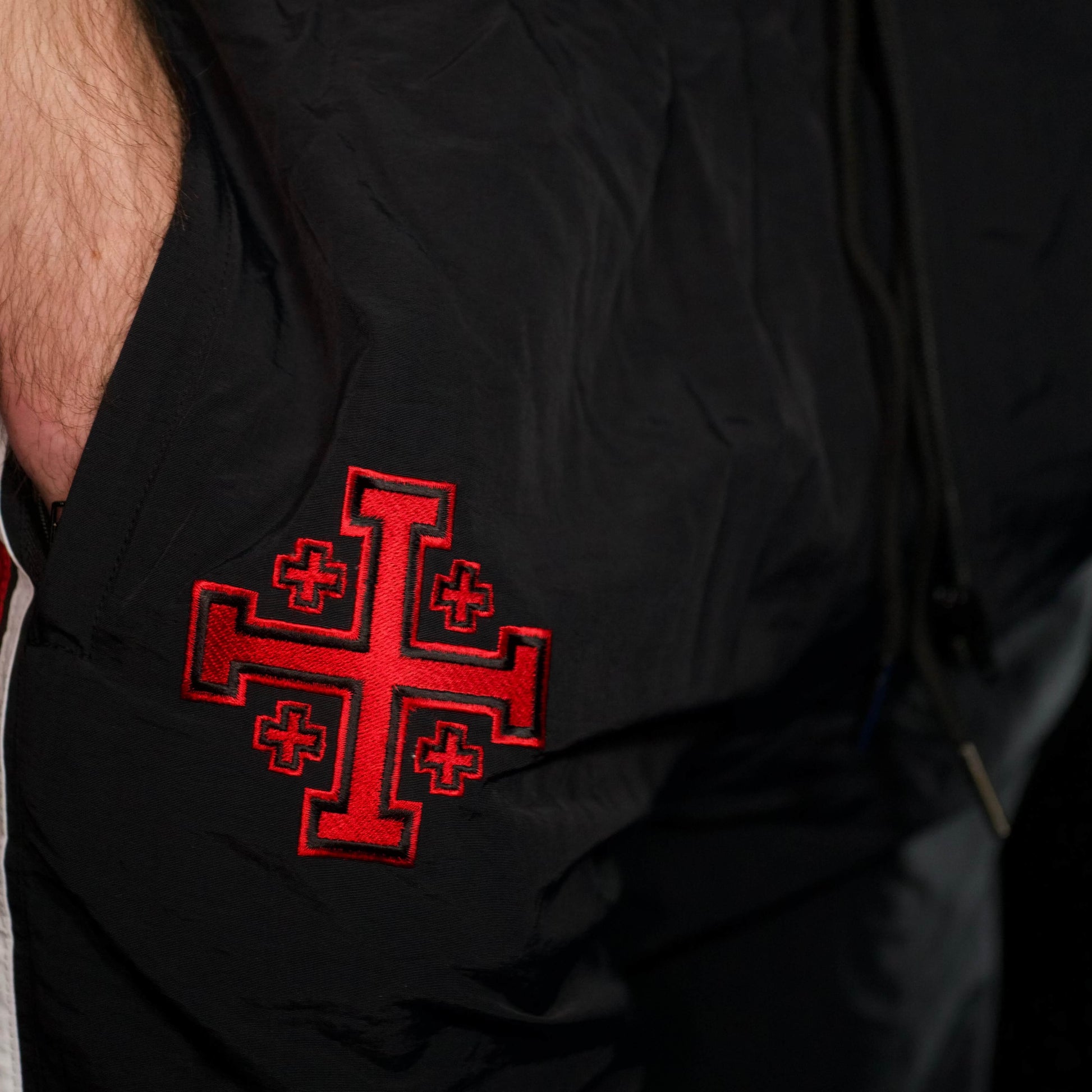 Black tracksuit pants with a red cross emblem on the pocket.