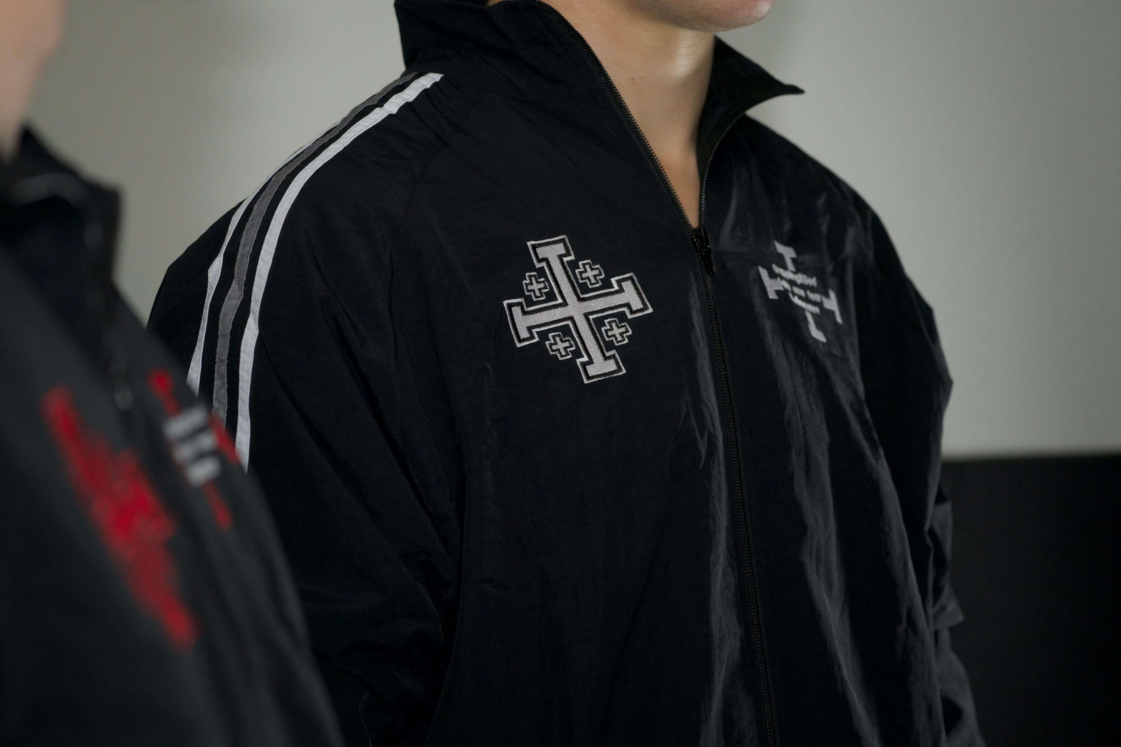Person wearing a black jacket with a cross emblem on a plain background