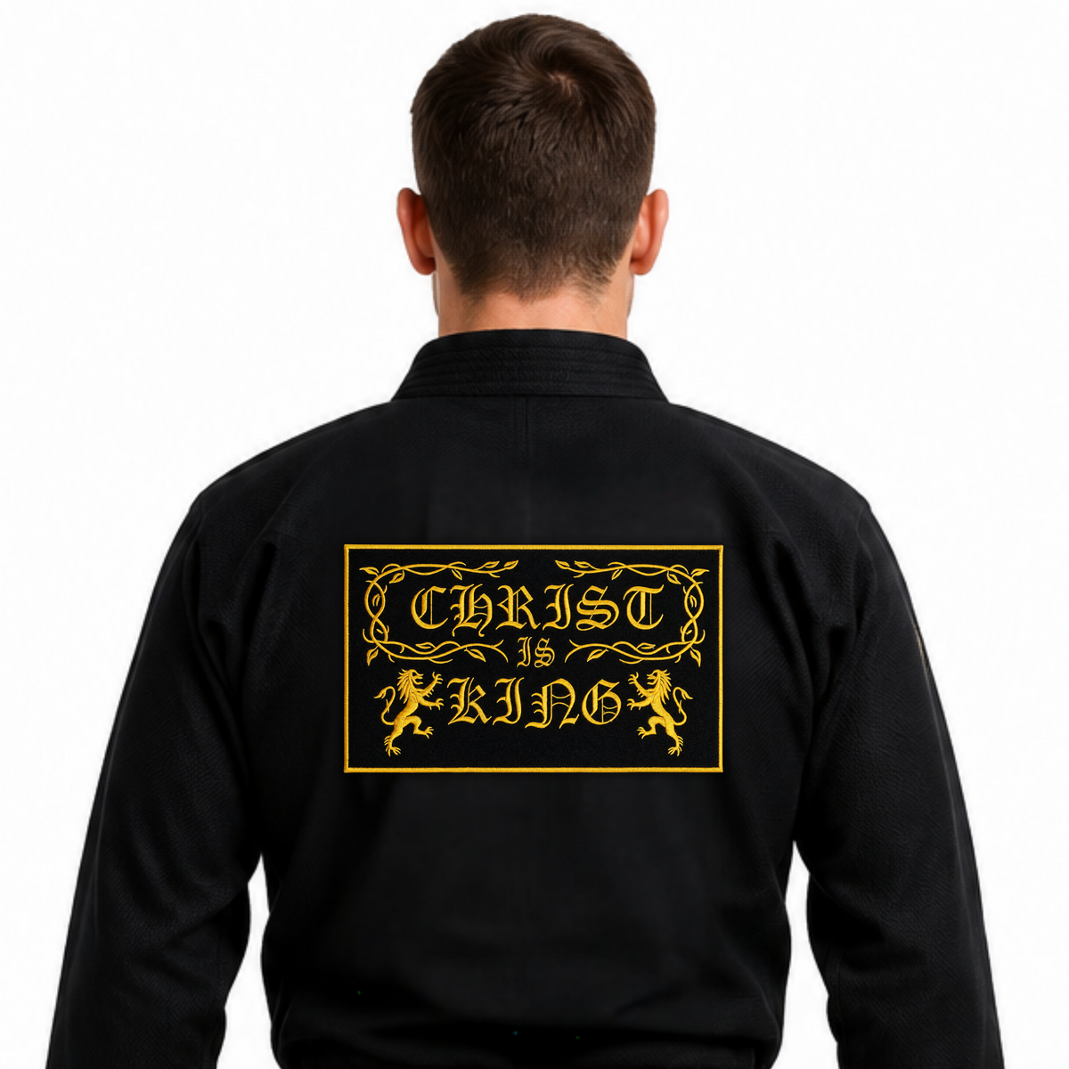 A man viewed from the back wearing a black martial arts gi with a black belt, featuring a large gold graphic on the back that reads 'CHRIST IS KING' with decorative borders and lions.