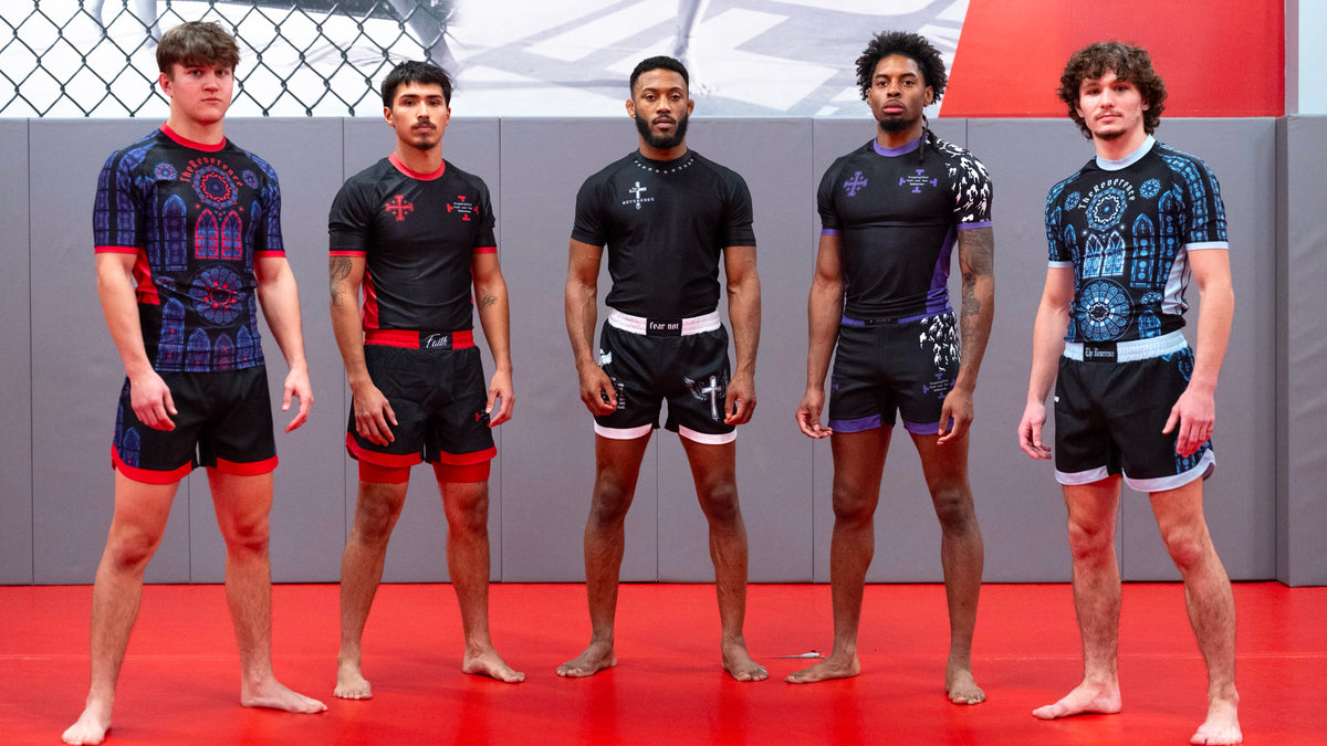Five male athletes standing in a row on a red mat inside a gym, wearing black and blue patterned fight shirts and black fight shorts with red, white, and purple accents.