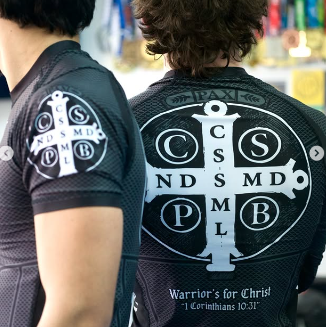 Two people wearing black shirts with white logos and text, standing back-to-back.