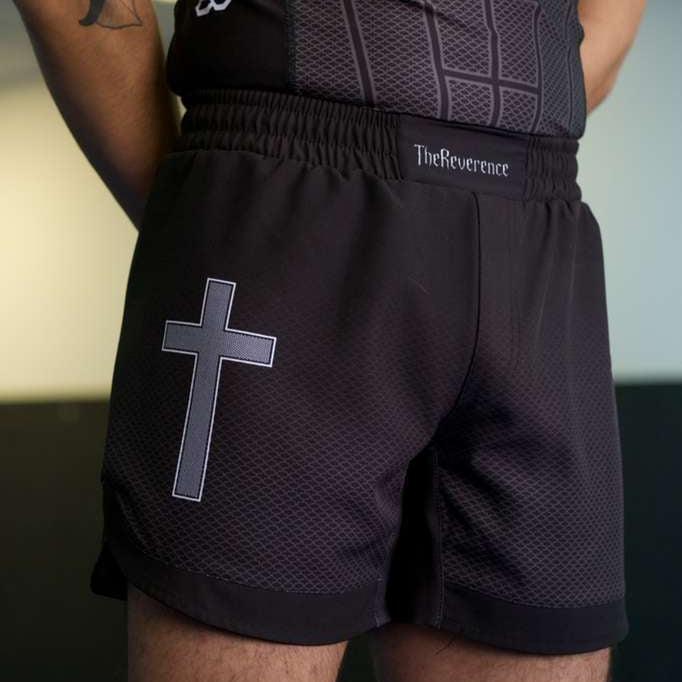 Person wearing black athletic shorts with a cross design and a matching top, with 'The Reverend' branding.