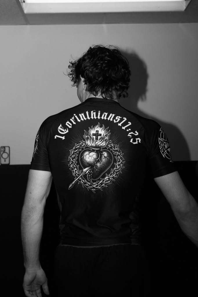 Person wearing a black t-shirt with a design and text on the back, standing against a plain wall.