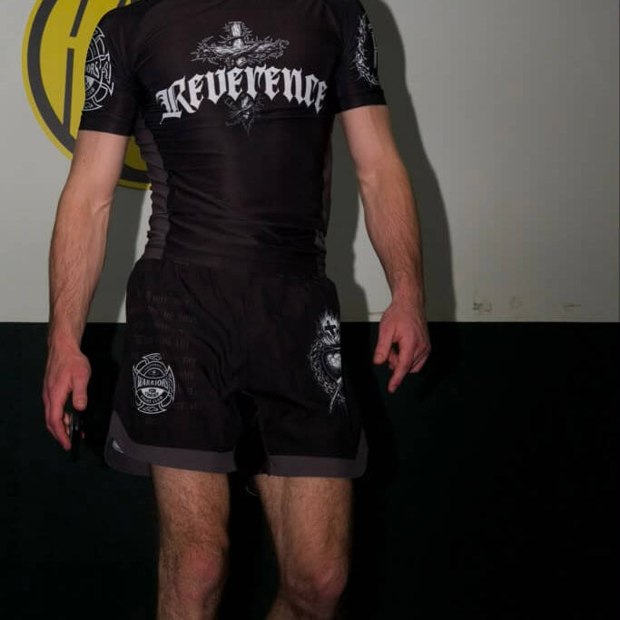 Person wearing a black 'Reverence' shirt and shorts in a room with a logo on the wall.